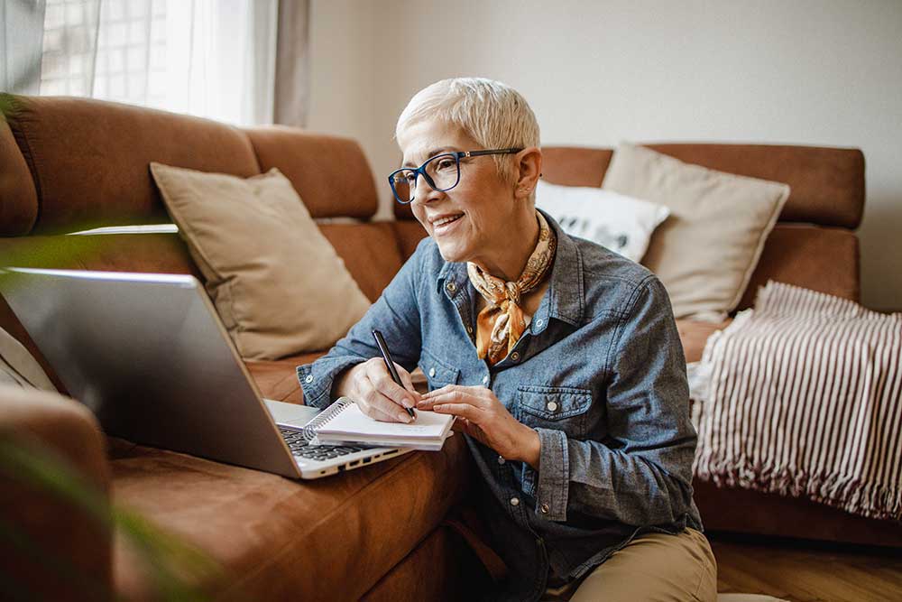Older female looking at laptop taking notes
