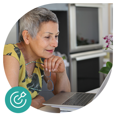 Senior woman using a laptop, wearing a yellow floral top, thoughtful expression.