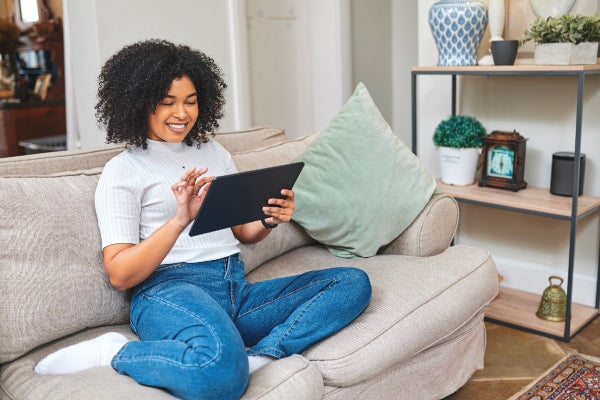 Smiling woman using a tablet on a beige sofa in a cozy living room.