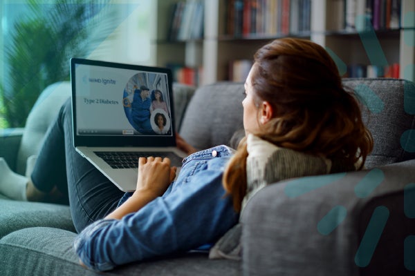 Woman on couch with laptop, video chat on screen, cozy living room.