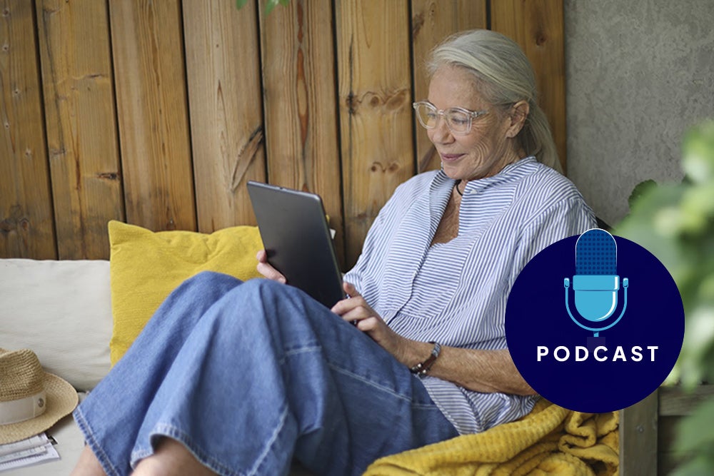 Elderly woman reading a tablet, sitting on a wooden bench.
