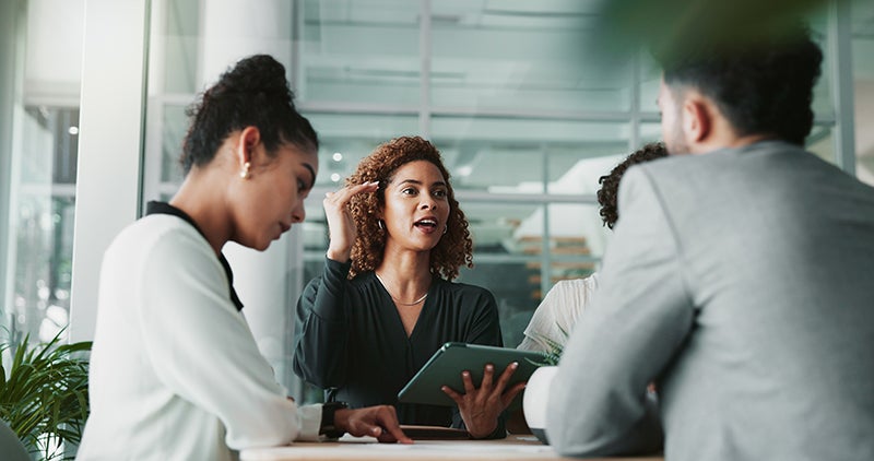 Group of colleagues in a meeting, one woman speaking while others listen attentively.