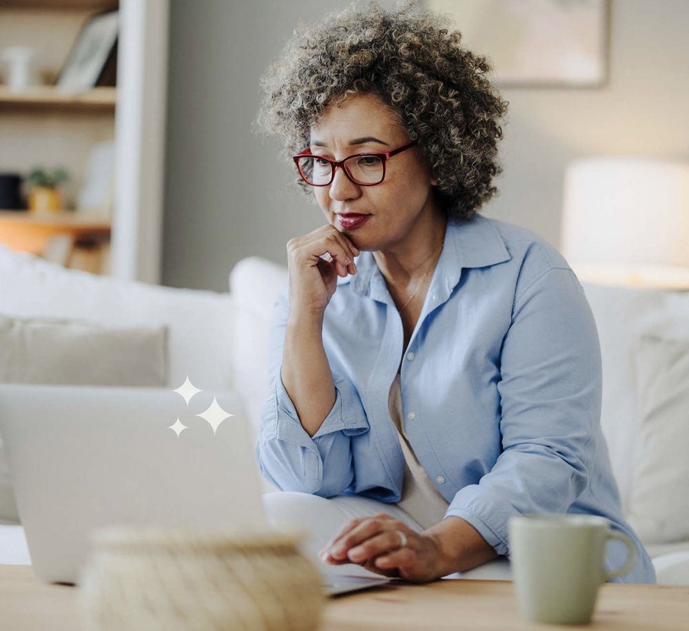 Woman in glasses working on a laptop at home, thoughtful expression.